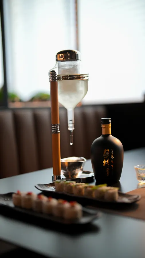 Chilled sake dispenser and bottle beside maki platters