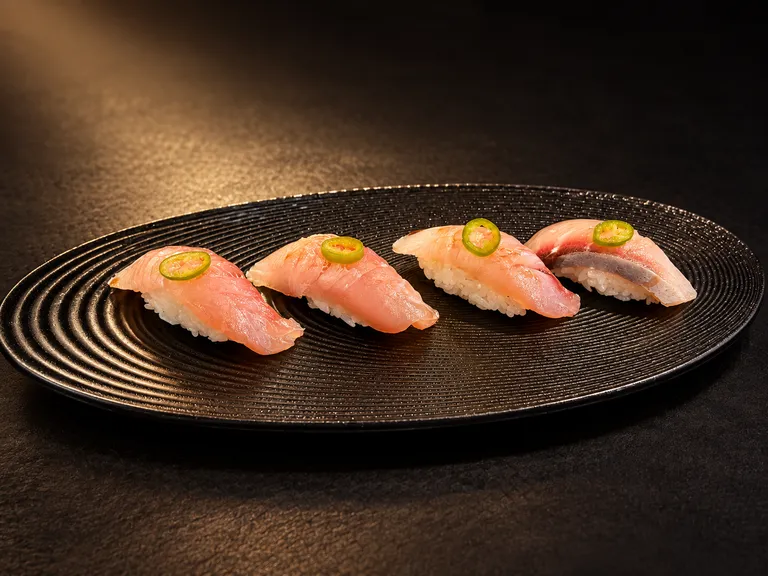 Four pieces of yellowtail Hamachi Nigiri with sliced chili on a black platter