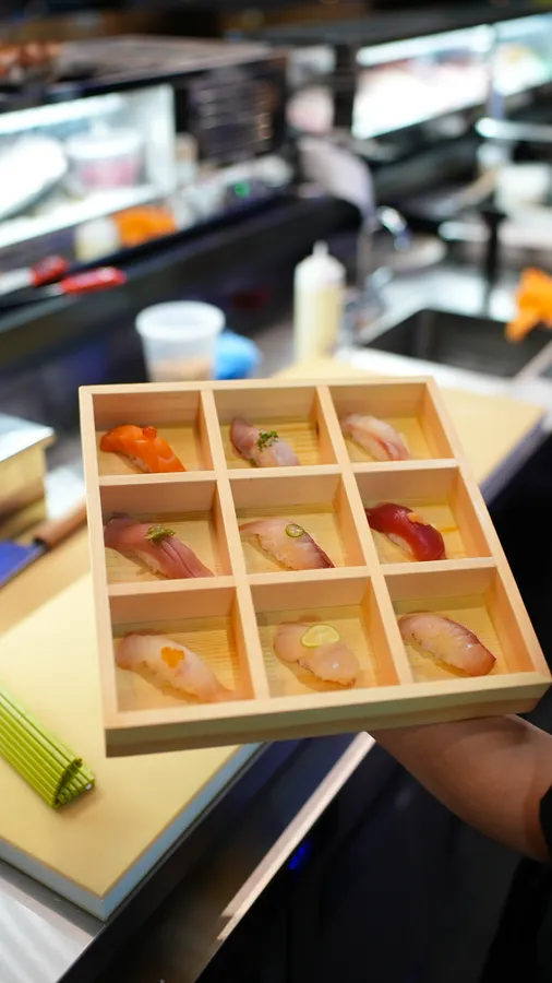 Nine assorted nigiri presented in a divided wooden tasting box