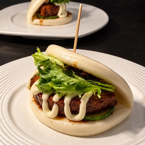 Niku Bun with pork chashu, sauce, and mixed greens on a white plate