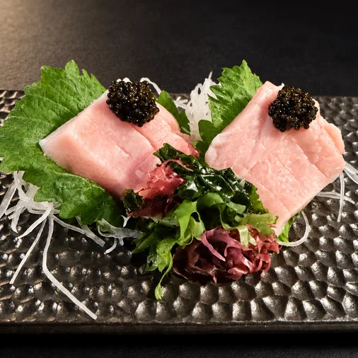 Two slices of otoro sashimi topped with caviar on a black platter