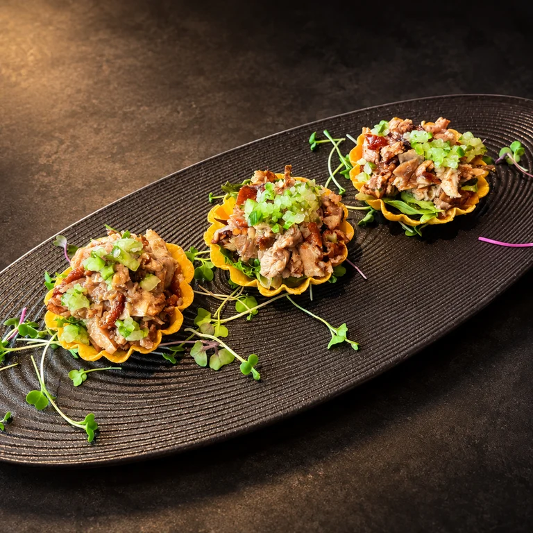 Three roasted duck tartlets with greens and diced cucumber on a black platter