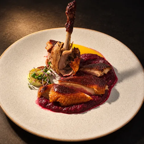 Roasted duck breast and leg over beet purée with sauce on a white plate