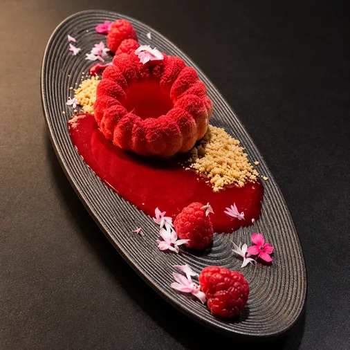 Red panna cotta with raspberries and fruit sauce on a black platter