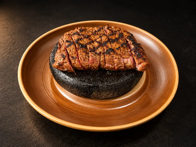 Sliced grilled Spinalis ribeye cap on a hot stone and bronze plate