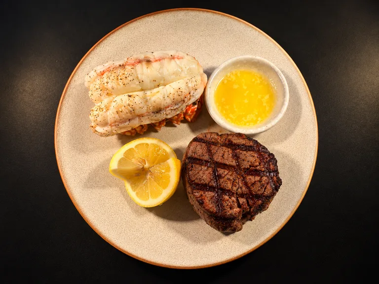 South African lobster and grilled filet served with lemon and melted butter on a ceramic plate