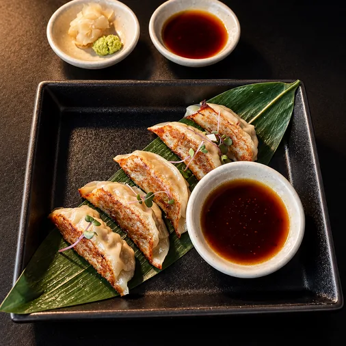 Wagyu Gyoza dumplings with dipping sauce on a black platter